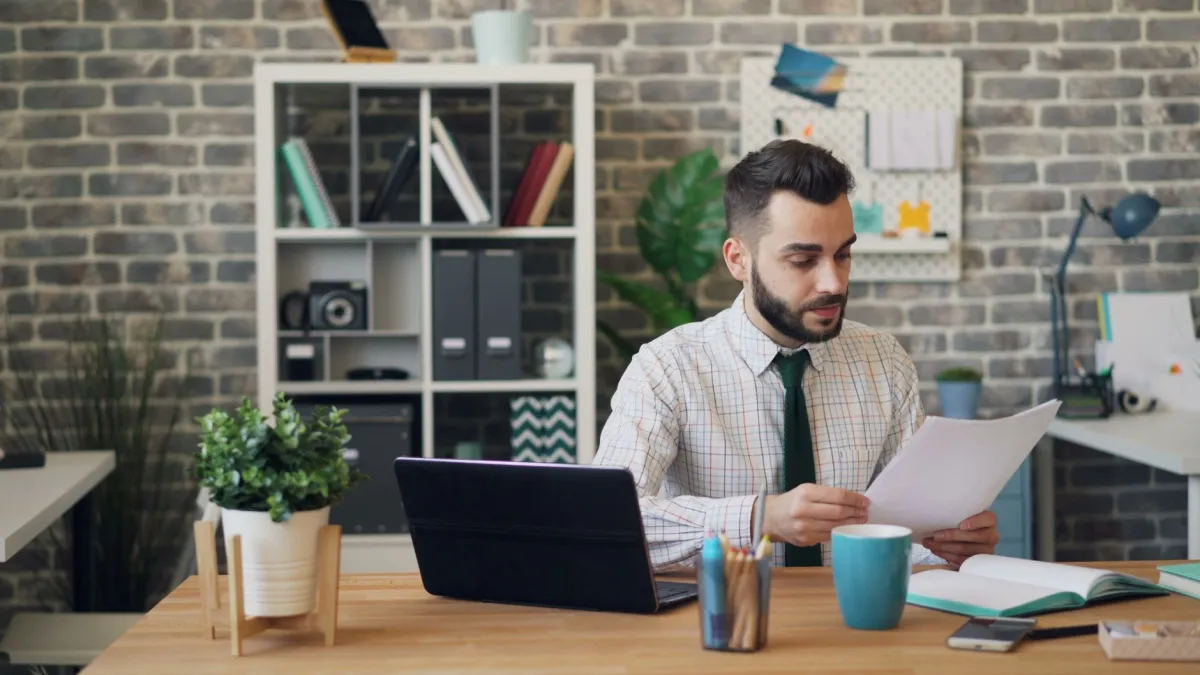 bearded, bookshelf, business, businessman, coffee, coffee mug, commercial, company, corporate, desk, documents, enterprise, laptop, man, office, office worker, professional, reading document, reviewing, shirt, shirt tie, tie, wooden, workspace